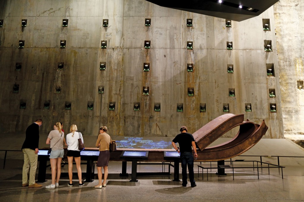 Visitors write messages on interactive tables in front of a steel column from the South Tower, folded over onto itself during the tower’s collapse on 9/11. Photo: Jin Lee/911 Memorial.