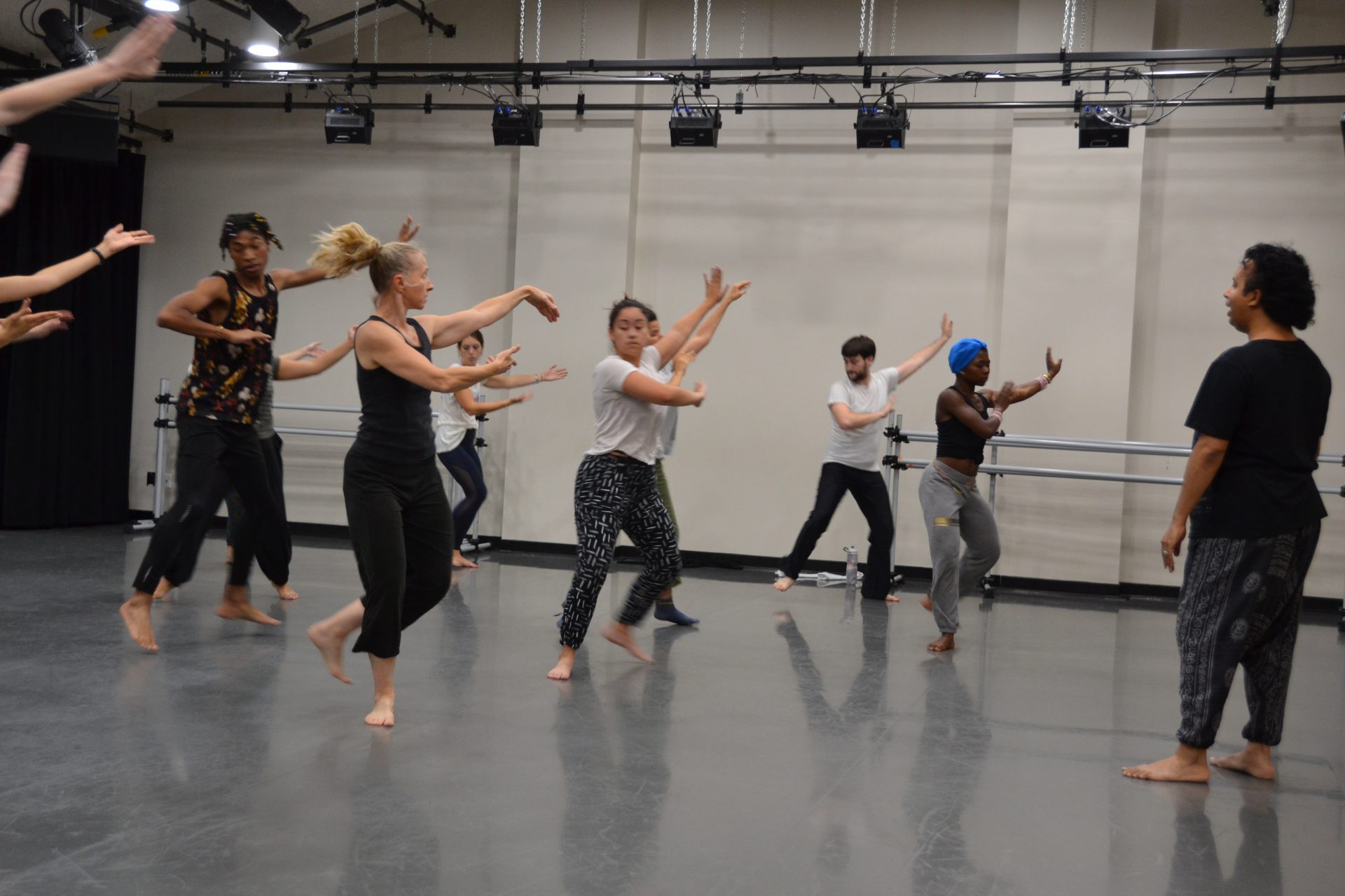 Hari is in front of the class; the students are dancing with arms out, some in the middle of a leap.