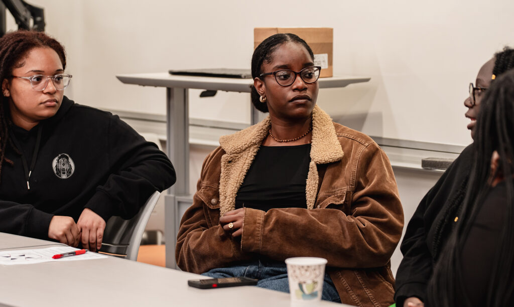 Three women of color sitting and engaged in discussion in a classroom.