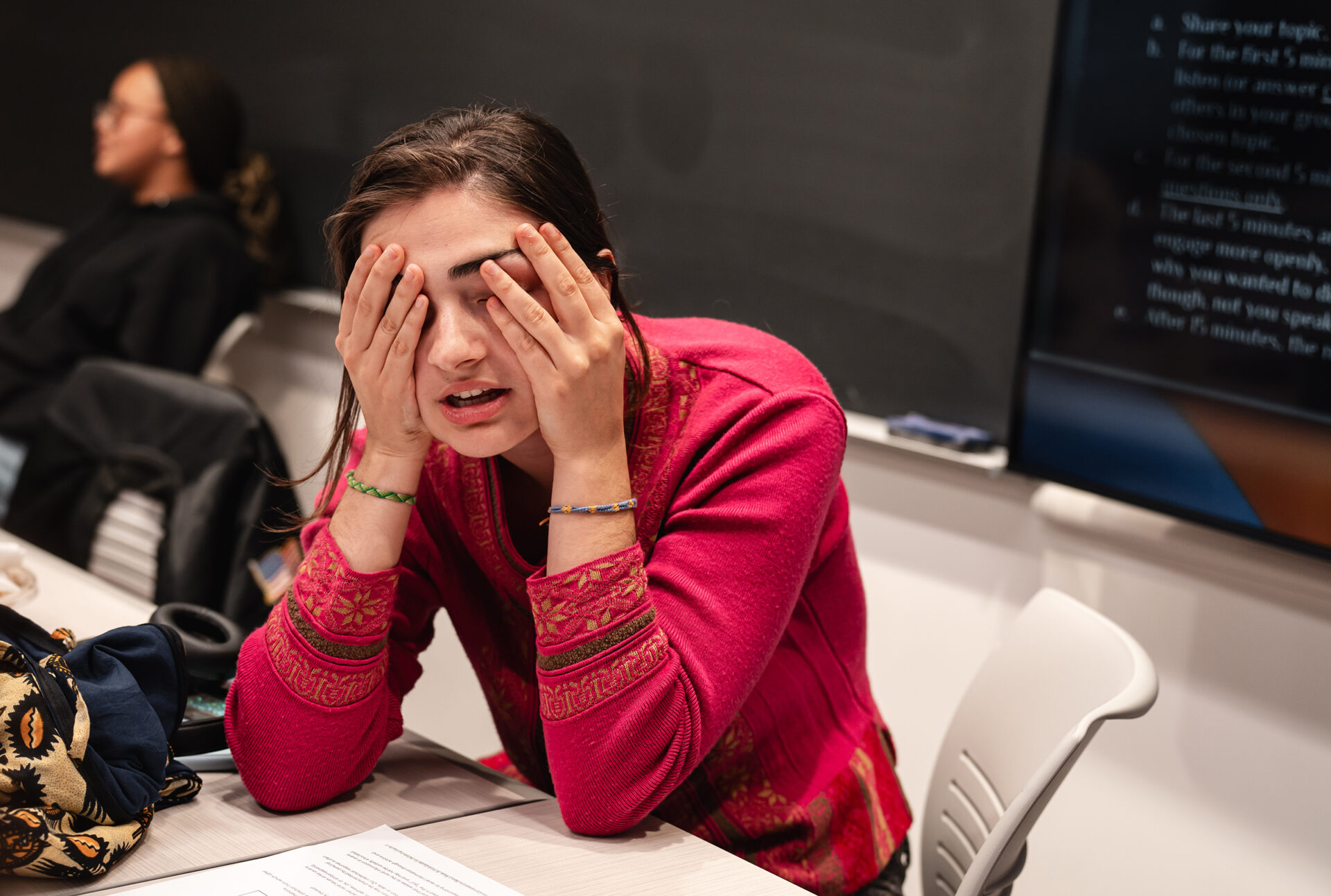 Young woman with face in hands during classroom discussion.